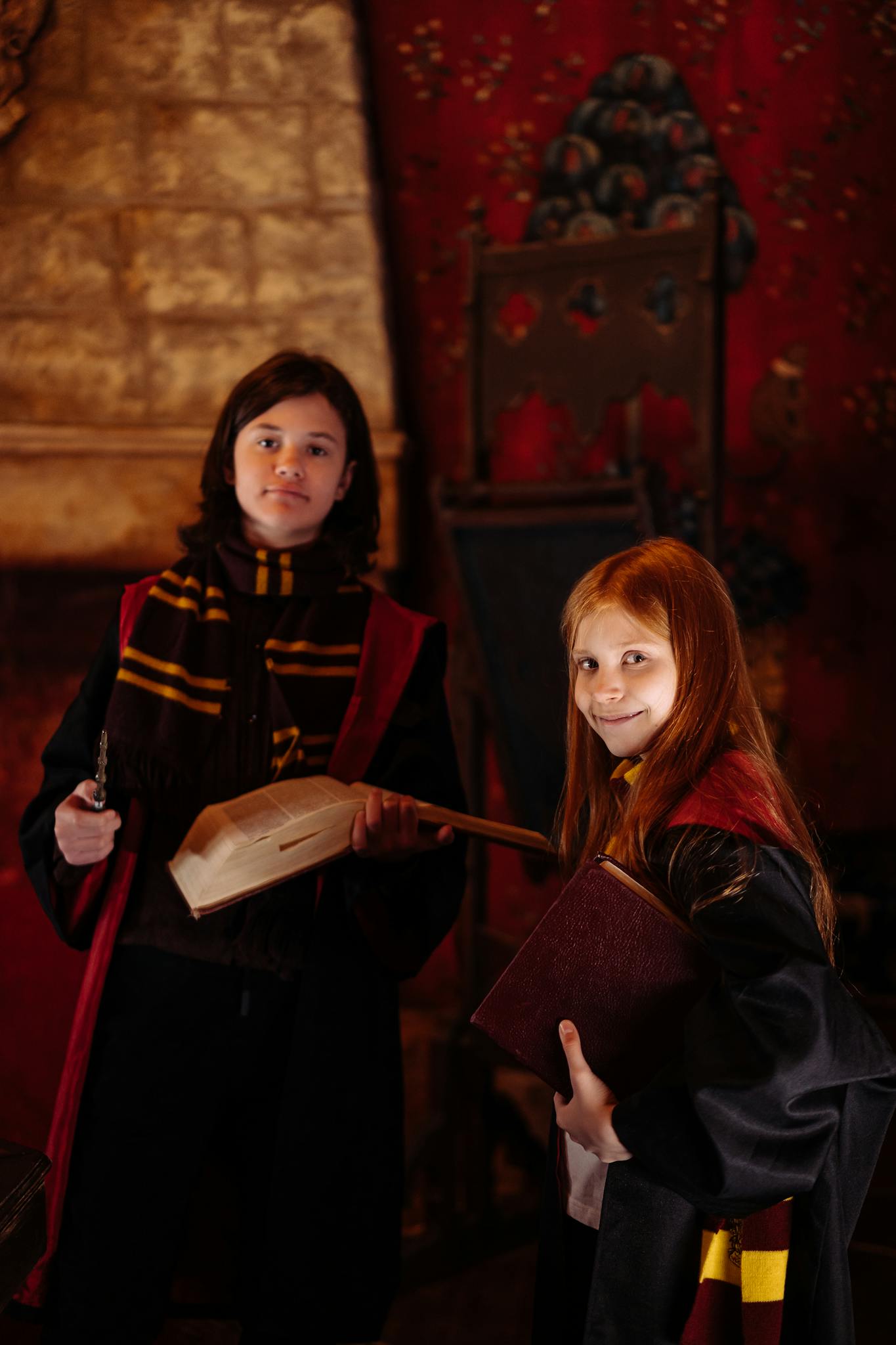 Two students in wizard costumes holding a wand and book in a magical setting.